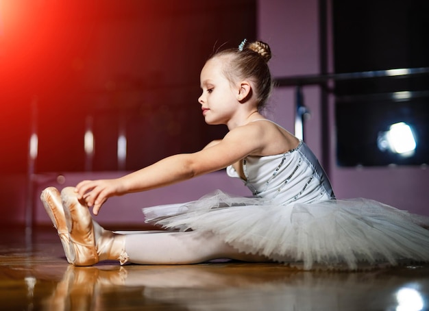 Foto di una piccola ballerina carina seduta in tutù bianco che mostra la flessibilità Primo piano della foto laterale