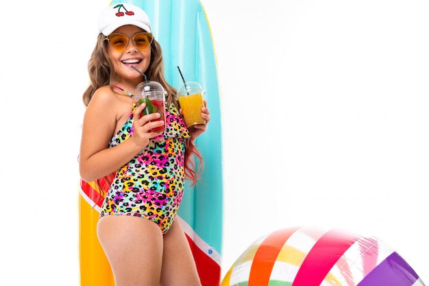 Foto di una ragazza affascinante in costume da bagno su un bianco, un bambino con frutta e un cocktail in mano, bevande analcoliche