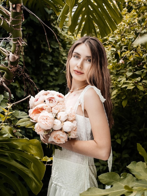 Foto di una ragazza che indossa un vestito e tiene in mano delle peonie in una serra. messa a fuoco selettiva