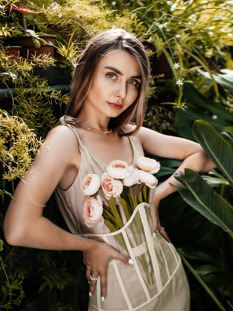 Foto di una ragazza che indossa un vestito e tiene in mano delle peonie in una serra. messa a fuoco selettiva