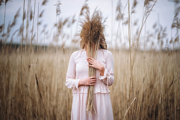 Foto di una ragazza con lunghi capelli biondi ricci in luce lunghi drees in piedi in un campo di canna