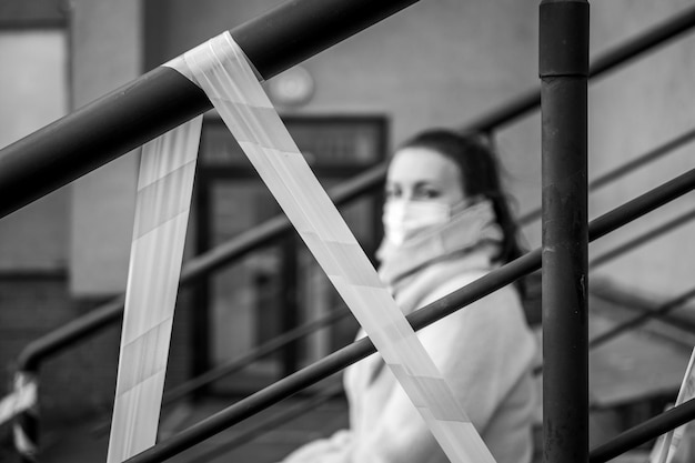 Foto di una ragazza con una maschera seduta per strada con nastri di avvertimento di pericolo