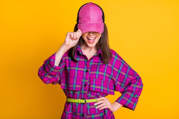 Foto di una ragazza dai capelli castani allegri che copre il viso indossa un cinturino di camicia rosa con copricapo isolato su uno sfondo di colore giallo brillante