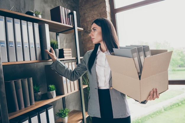 Foto di una ragazza frustrata titolare di una start-up che perde azienda in bancarotta raccoglie scaffali documenti archivi statistiche tenere scatola di cartone indossare giacca giacca blazer nella postazione di lavoro