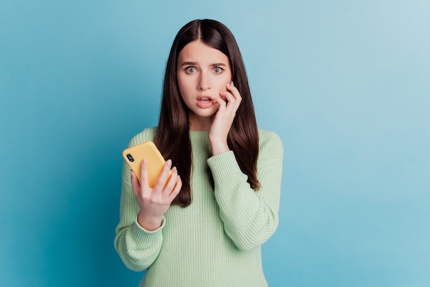 Foto di una ragazza preoccupata che tiene le unghie con il morso del telefono isolate su sfondo blu