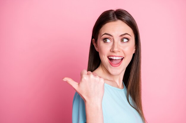 Foto di una ragazza sorpresa che punta il dito del pollice indossa un abito blu isolato su uno sfondo di colore rosa