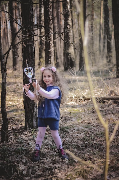 Foto di una ragazza sorridente con un cerchietto che gioca con un cuore di legno nella foresta
