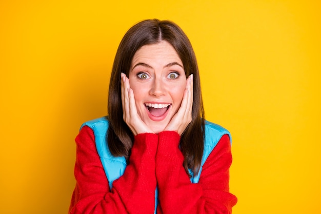 Foto di una ragazza stupita hipster che tocca il viso con le mani impressionato da un meraviglioso affare di stagione indossa un maglione rosso isolato su uno sfondo di colore brillante brillante