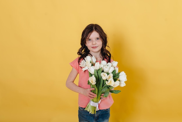 Foto di una ragazza su sfondo giallo con in mano un mazzo di tulipani bianchi come regalo che lei wil