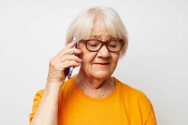 Foto di una vecchia signora in pensione con gli occhiali alla moda con uno smartphone in mano su sfondo chiaro