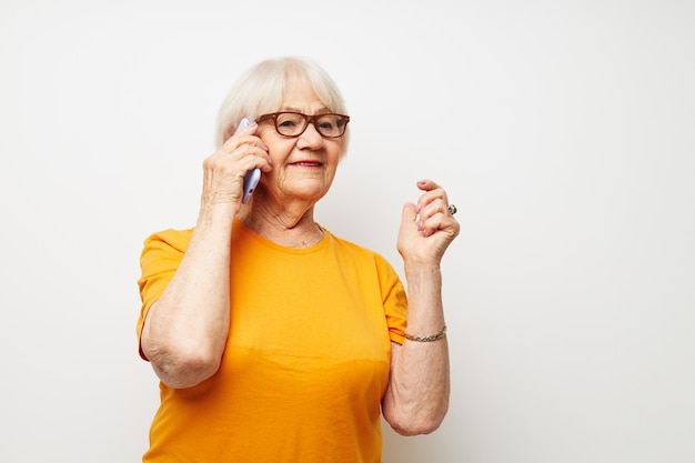 Foto di una vecchia signora in pensione con una maglietta gialla che posa la comunicazione tramite la vista ritagliata del telefono