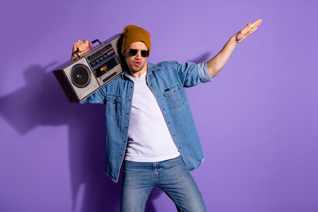 Foto di uomo incurante che balla con la musica dei bassi ad alto volume che indossa jeans denim camicia bianca isolata su sfondo di colore vibrante viola viola