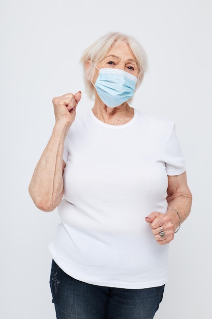 Foto di vecchia signora in pensione in maglietta casual e maschera medica sfondo chiaro