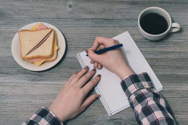 Foto di vista superiore in prima persona delle mani della donna che tengono la penna sulla piastra del blocco note