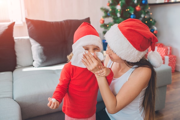 Foto divertente della donna si siede oltre a suo figlio e si copre la bocca con un tovagliolo bianco. La famiglia è ammalata a Natale.