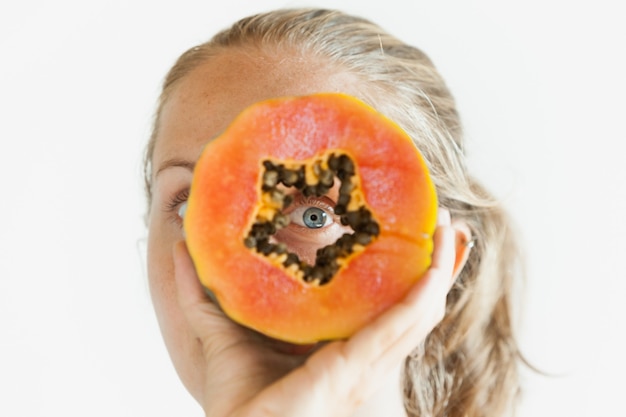 Foto divertente della giovane donna positiva con il fronte sorridente che tiene nelle mani la frutta tropicale matura - fetta arancione della papaia