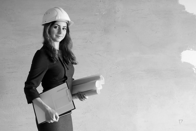 Foto in bianco e nero di una donna architetto in cantiere con disegni e taccuino