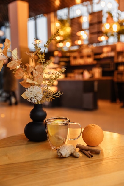 Foto in primo piano di un bicchiere trasparente di tè allo zenzero su un tavolo in un caffè Zenzero arancione e cannella come ingredienti della bevanda Tè della salute