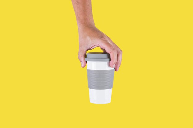 Foto in studio con sfondo giallo di una mano che tiene una tazza di caffè in plastica per andare