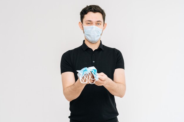 Foto in studio di un giovane che indossa una maschera protettiva con in mano molte maschere mediche