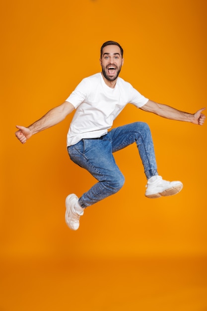 Foto integrale del ragazzo non rasato in maglietta e jeans che salta e che si diverte, isolato