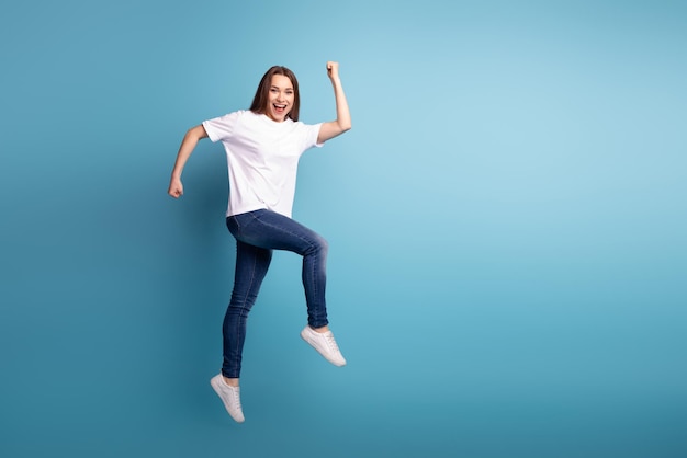 Foto laterale del profilo a figura intera di una giovane ragazza eccitata che corre la stagione del salto di punta isolata su sfondo blu