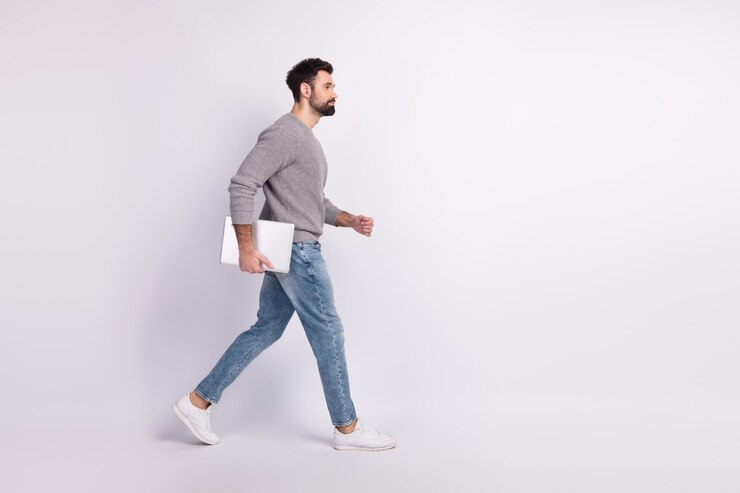 Foto laterale del profilo del corpo completo del rappresentante del laptop della presa a piedi del giovane isolato su uno sfondo di colore grigio