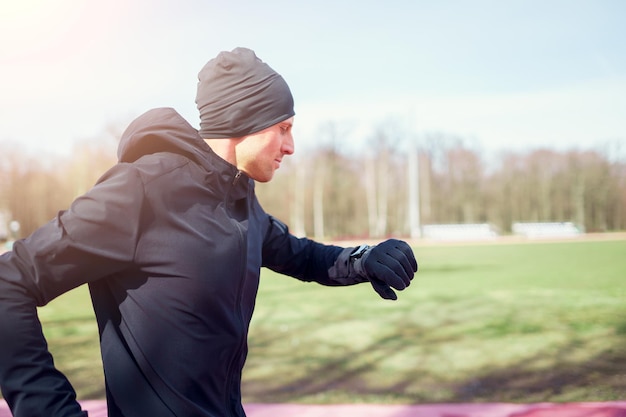 Foto laterale dell'uomo che corre in abiti neri nel pomeriggio di primavera.