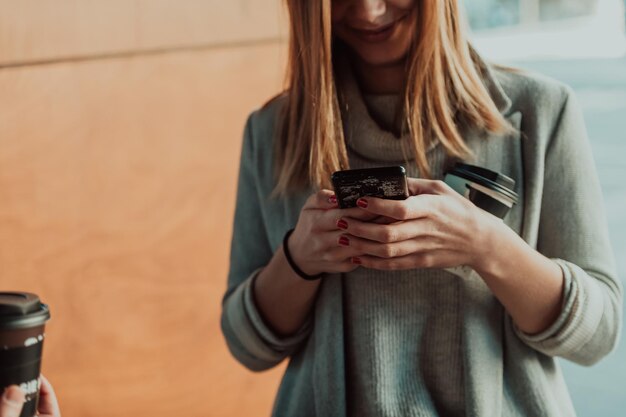 foto macro di una ragazza che beve caffè e usa un telefono cellulare durante una pausa dal lavoro.