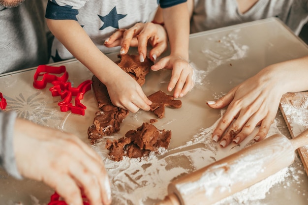 Foto, mani ravvicinate di padre, madre e figlio cuociono i biscotti. Disporre su una teglia, ritagliare con gli stampini per biscotti. Tempo felice con la famiglia. Momenti di Natale. La famiglia si diverte.