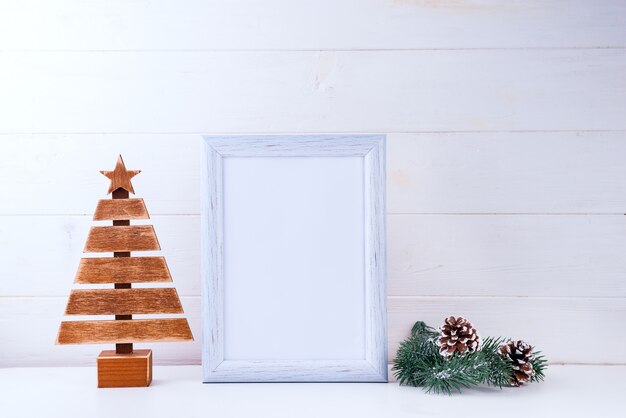 Foto mock up con cornice bianca, albero di legno e rami di pino su legno bianco