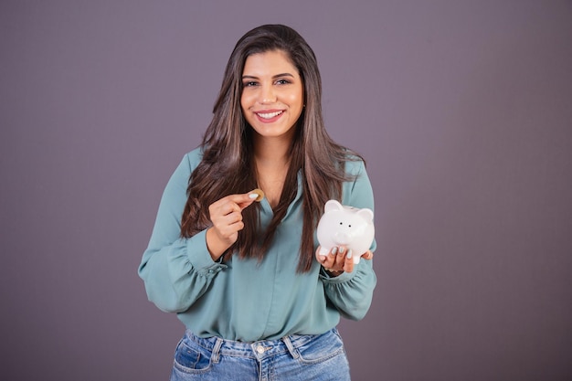 Foto orizzontale Bella donna brasiliana con abiti casual Jeans e camicia verde azienda salvadanaio e moneta Finanza