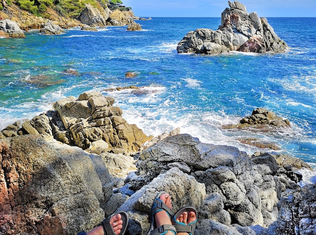 Foto panoramica della costa rocciosa con i piedi dei turisti in sandali donne e uomini Il concetto di fare escursioni alla gente comune lungo la costa