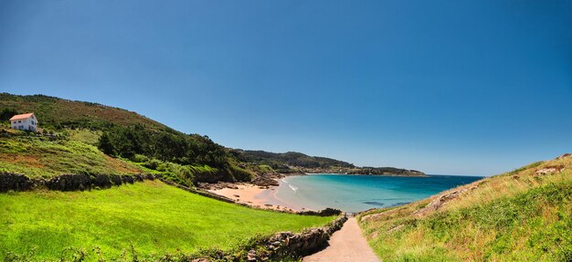 Foto panoramica di una spiaggia con acqua cristallina e una casa e vegetazione Porto do Son Galicia