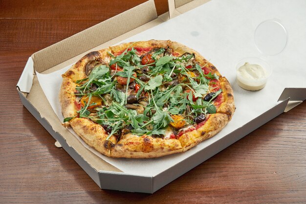 Foto per la consegna della pizza. pizza vegetariana con olive, formaggio fuso, rucola, funghi, pomodorini