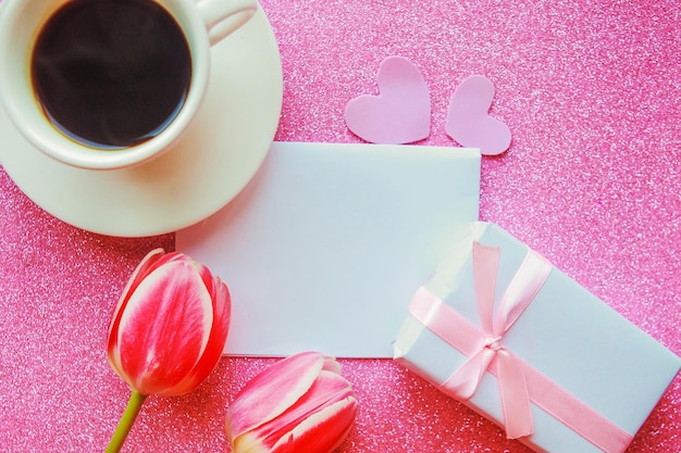 Foto piatta con scatola regalo di tazza di caffè e tulipani rossi su sfondo rosa Bella Giornata delle Madri Giorno delle Donne o Valentino biglietto di auguri Modello di biglietta di auguri Giorno delle Madri