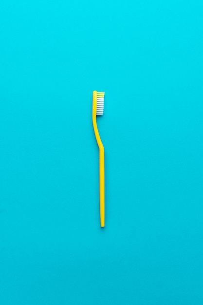 Foto piatta minimalista dello spazzolino da denti giallo su sfondo blu turchese