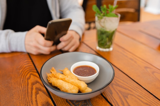 foto ravvicinata delle mani dell'uomo al tavolino con mangiare e bere, utilizzando lo smartphone