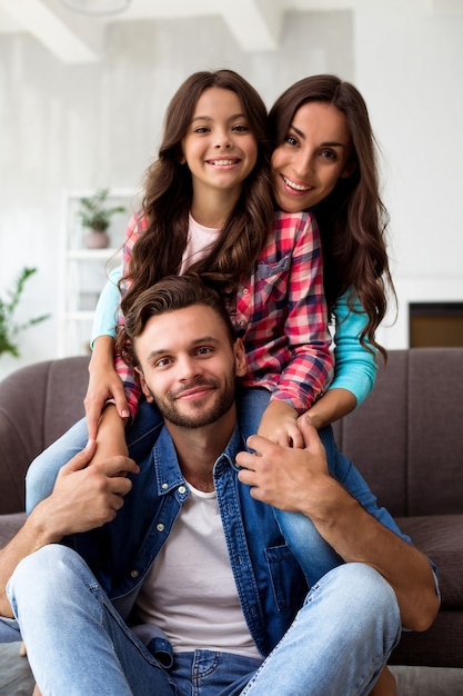 Foto ravvicinata di madre, padre e figlia che posano insieme per una foto comune nel loro elegante soggiorno, abbracciati con sorrisi radiosi