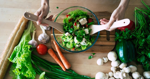 Foto ravvicinata di mani femminili durante la preparazione e il taglio degli ingredienti in insalata vegana in cucina a casa