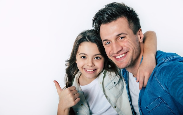 Foto ravvicinata di un giovane papà e del suo bambino, che si abbracciano teneramente e sorridono, mentre guardano insieme la fotocamera.