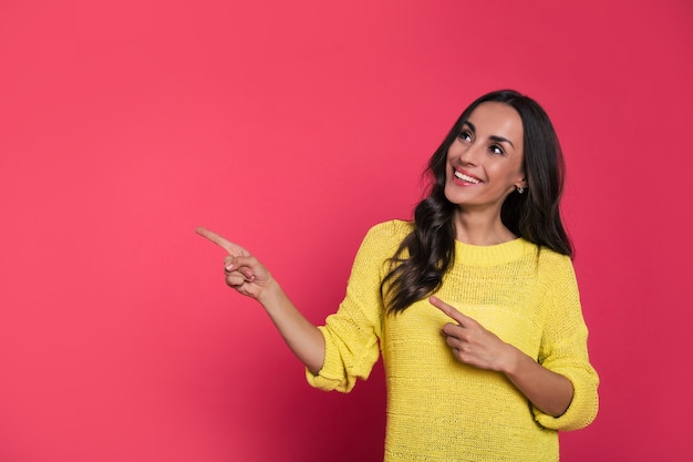 Foto ravvicinata di una bella ragazza con un maglione lavorato a maglia, che guarda avanti e punta a sinistra con l'indice mentre sorride sinceramente