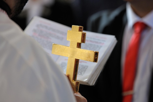 Foto ravvicinata di una croce ortodossa d'oro tenuta da un sacerdote durante una cerimonia religiosa