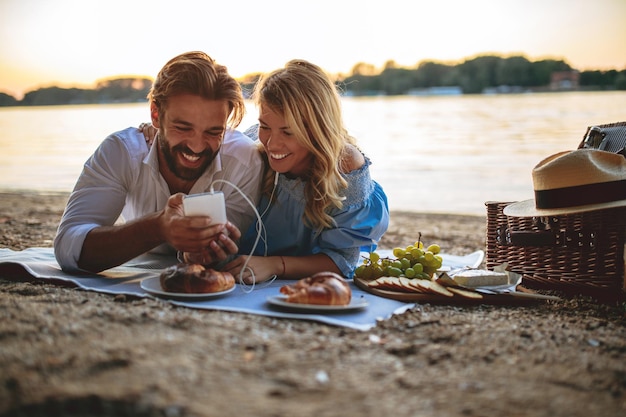 Foto ravvicinata di una giovane coppia che usa il telefono cellulare per ascoltare la musica durante un picnic