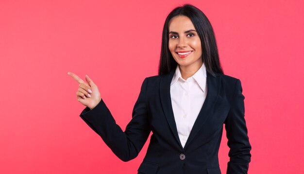 Foto ravvicinata di una giovane donna d'affari felice con lunghi capelli neri corvini, che posa con un abito nero, guarda nella telecamera e punta lontano