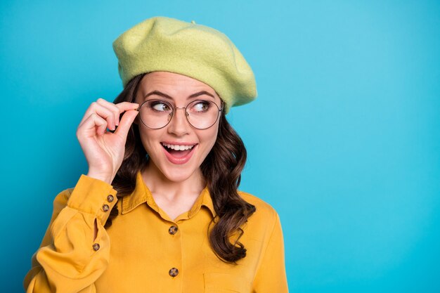 Foto ravvicinata di una ragazza allegra positiva e stupita che tocca gli occhiali impressionato da un meraviglioso affare novità indossa un copricapo isolato su uno sfondo di colore blu