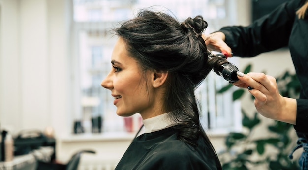 Foto ravvicinata di una splendida donna con bei capelli mossi, che si fa fare i capelli in un salone di bellezza.