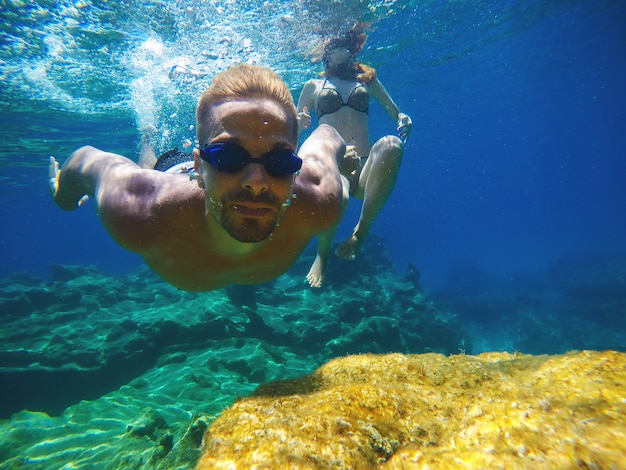 Foto ravvicinata subacquea di una giovane coppia di amore giocoso che nuota nel mare esotico turchese per le vacanze estive.