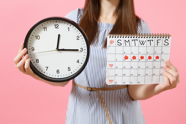 Foto ritagliata di donna in abito blu con orologio rotondo, calendario dei periodi per il controllo dei giorni delle mestruazioni isolati su sfondo rosa di tendenza. Concetto medico, sanitario, ginecologico. Copia spazio.