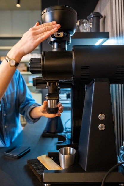 Foto ritagliata di un esperto impiegato di un caffè che macina i chicchi di caffè con un macinino elettrico